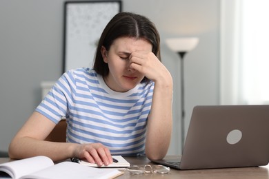 Overwhelmed woman sitting with laptop at table indoors