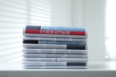 Newspapers with headline CYBER ATTACK stacked on white table indoors