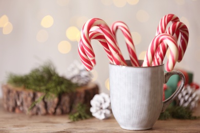 Photo of Christmas candy canes in cup on wooden table against blurred lights, space for text