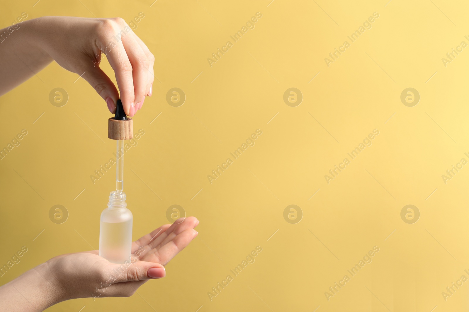 Photo of Woman dripping serum from pipette into bottle against pale orange background, closeup. Space for text