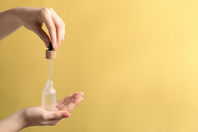 Photo of Woman dripping serum from pipette into bottle against pale orange background, closeup. Space for text