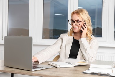 Lady boss talking on smartphone near laptop in office. Successful businesswoman