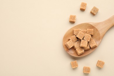 Brown sugar cubes in wooden spoon on beige background, top view. Space for text