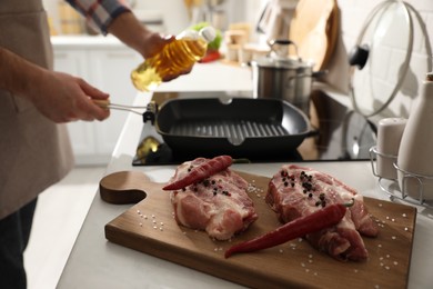 Photo of Man pouring cooking oil into frying pan, focus on raw meat