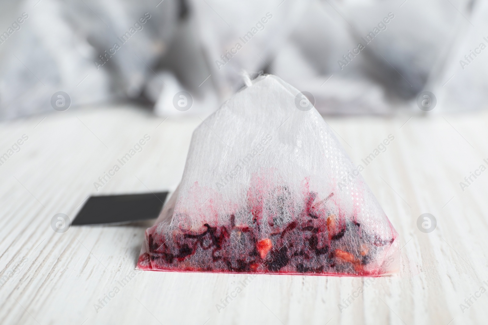 Photo of Used pyramid tea bag on white wooden table, closeup