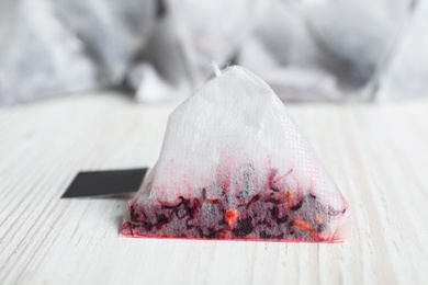 Photo of Used pyramid tea bag on white wooden table, closeup