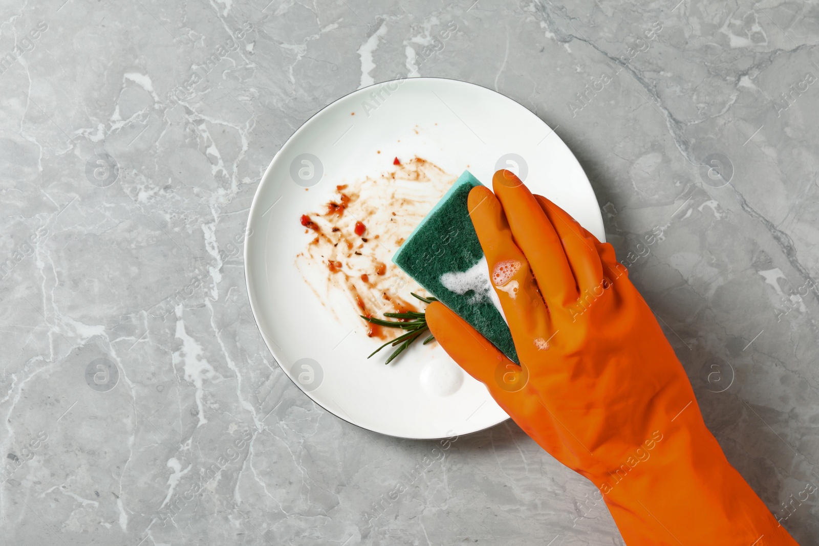 Photo of Woman washing dirty plate at grey marble table, top view