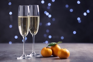 Photo of Sparkling wine in glasses near tangerines on grey table against blurred lights, space for text