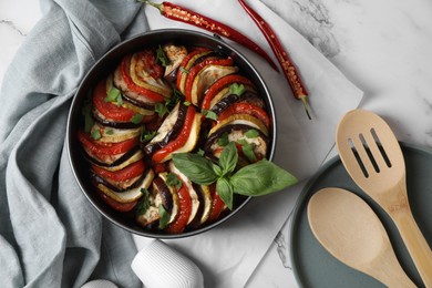 Photo of Delicious ratatouille, chili peppers, wooden spoon and spatula on white marble table, flat lay