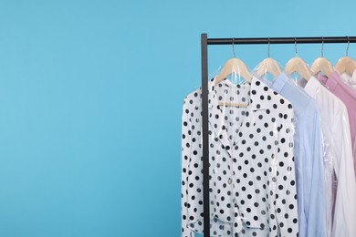 Dry-cleaning service. Many different clothes in plastic bags hanging on rack against light blue background, space for text