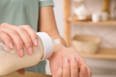 Photo of Woman checking temperature of infant formula indoors, closeup with space for text. Baby milk