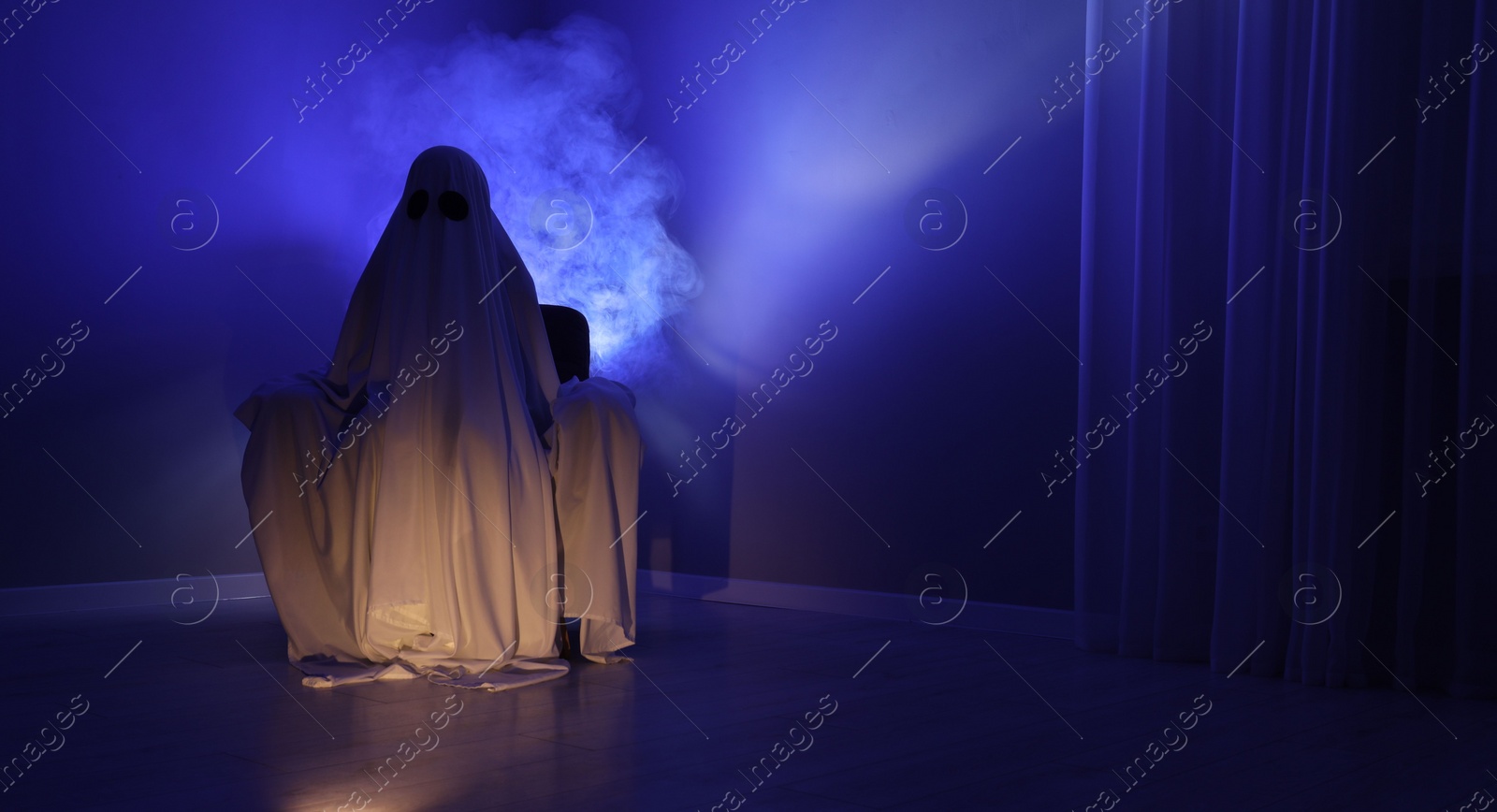 Photo of Creepy ghost. Woman covered with sheet sitting in armchair in blue light, space for text