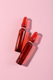 Photo of Glass ampoules with liquid on pink background, top view