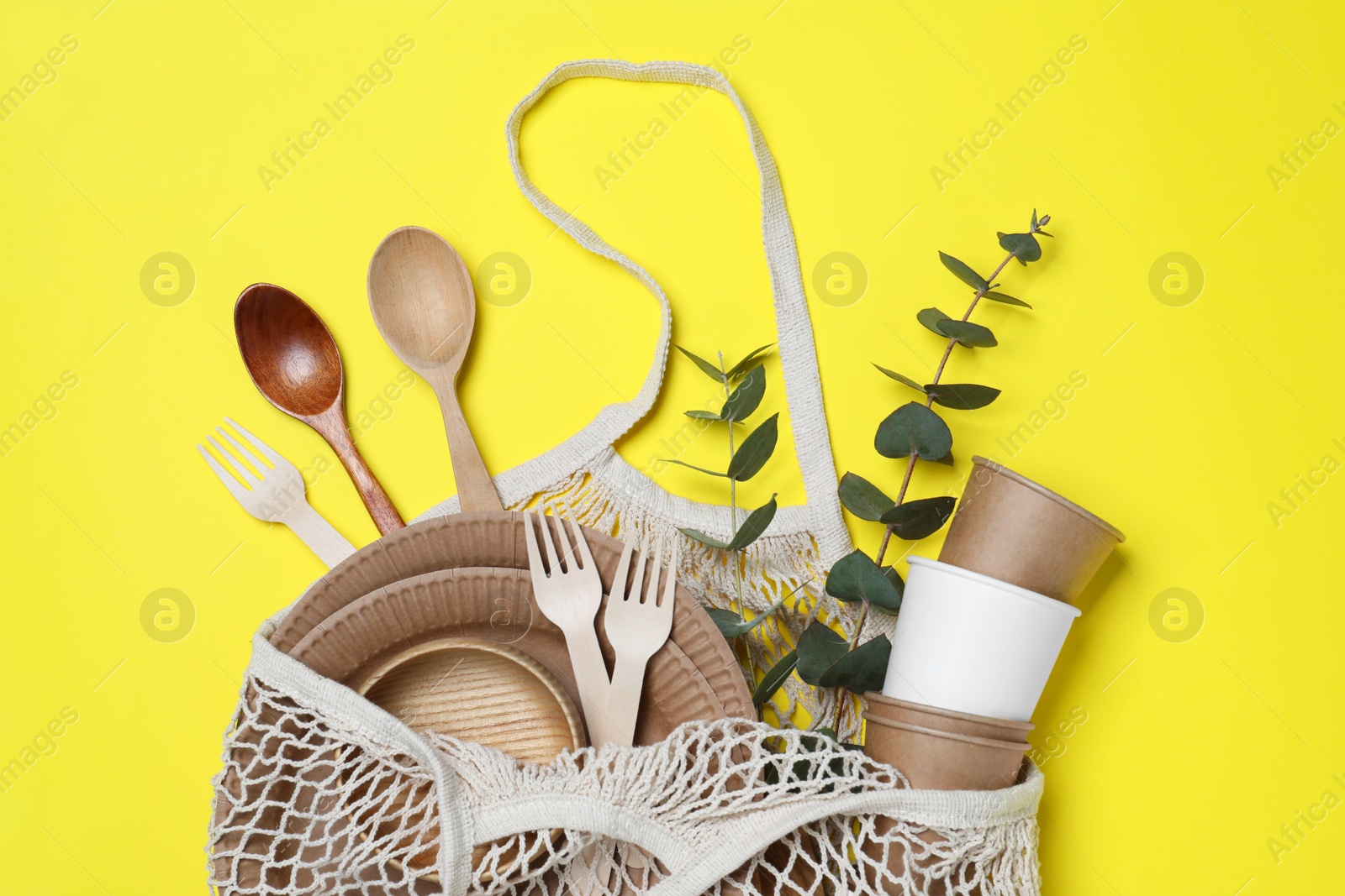 Photo of Net bag with different eco items on yellow background, top view. Recycling concept