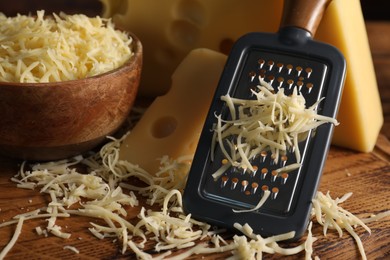 Photo of Grated, cut cheese and grater on wooden board, closeup