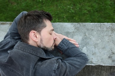 Photo of Tired man sleeping on stone parapet outdoors, top view. Space for text
