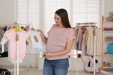 Happy pregnant woman choosing baby clothes in store. Shopping concept