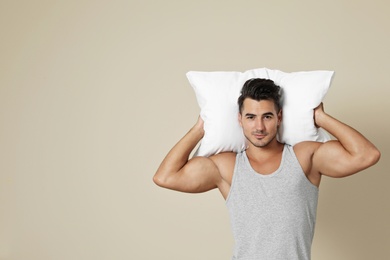 Young man with soft pillow on color background