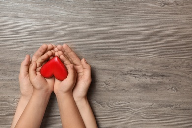 Photo of Woman and child holding heart on wooden background, top view with space for text. Donation concept