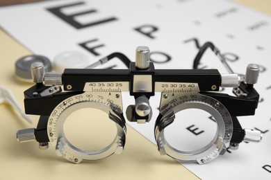 Photo of Trial frame with eye chart test on beige background, closeup. Ophthalmologist tools