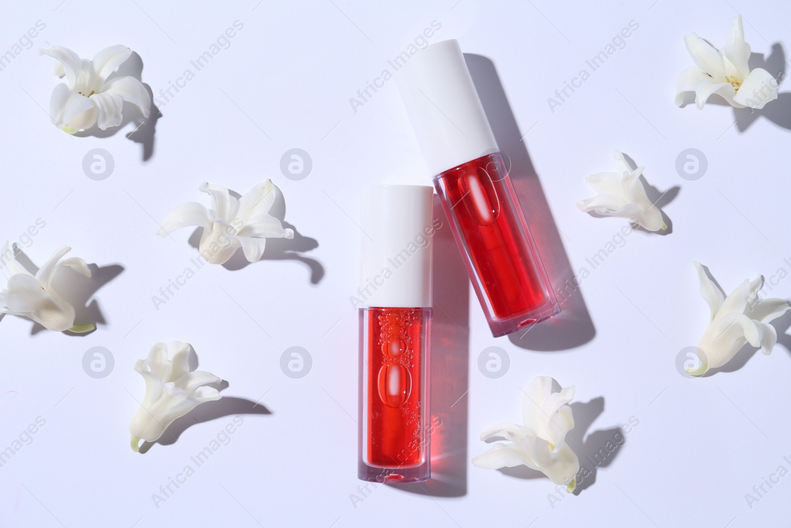 Photo of Bright lip glosses and flowers on white background, flat lay