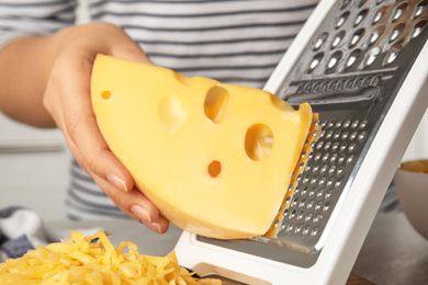 Woman grating fresh cheese at table, closeup