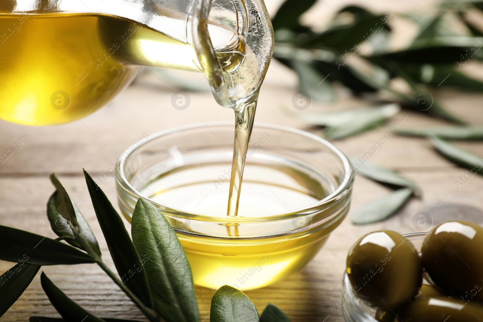 Photo of Pouring olive oil from jug into bowl on wooden table, closeup. Healthy cooking