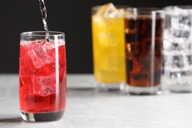 Pouring refreshing soda water into glass with ice cubes on white table, space for text