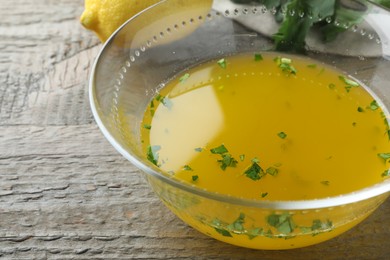 Bowl with lemon sauce on wooden table, closeup. Delicious salad dressing