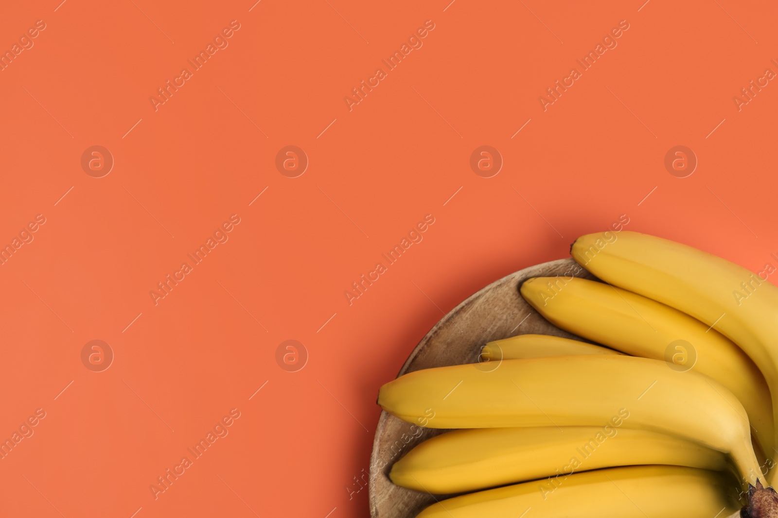 Photo of Ripe yellow bananas on coral background, top view. Space for text