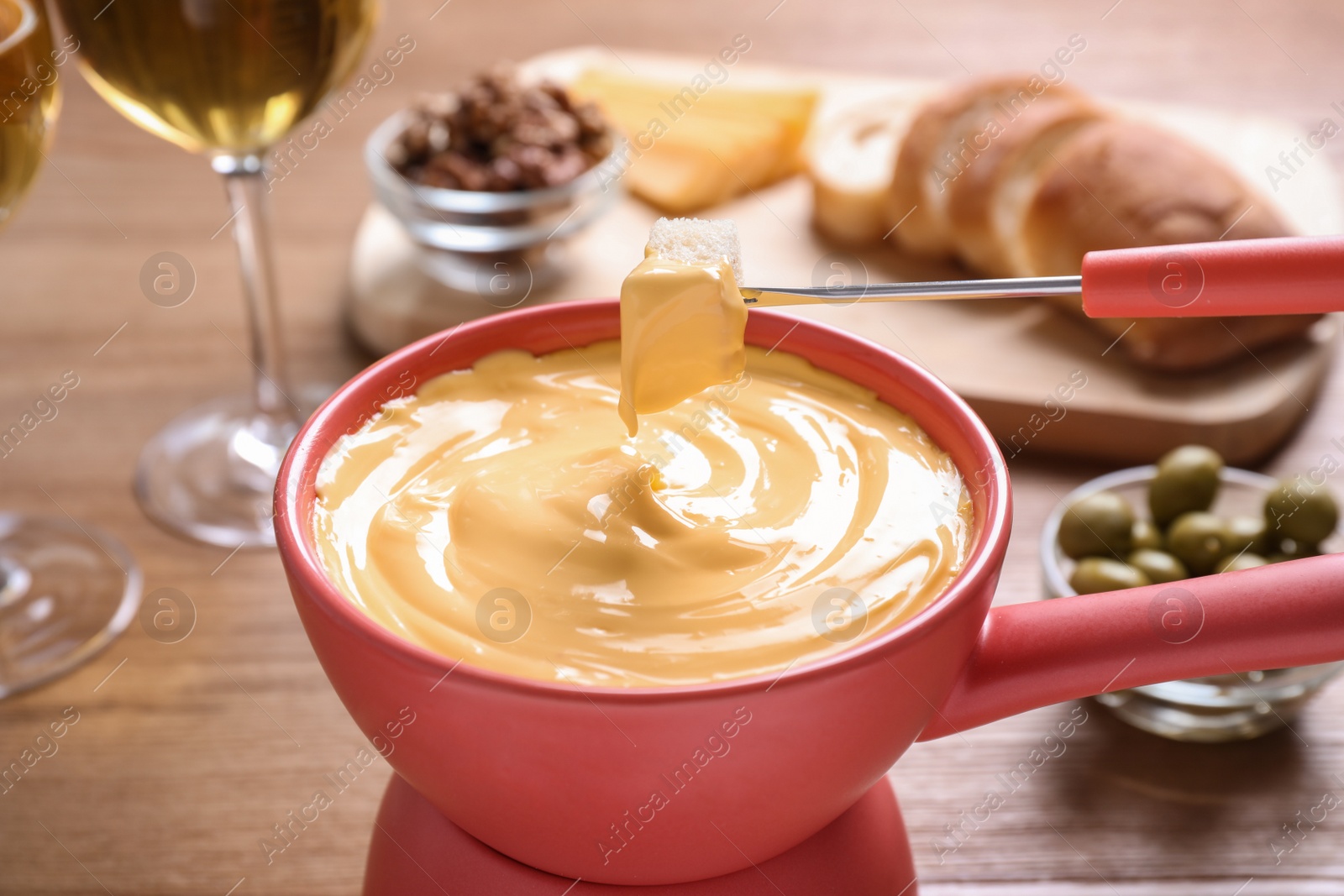 Photo of Dipping bread into pot with cheese fondue on table, closeup