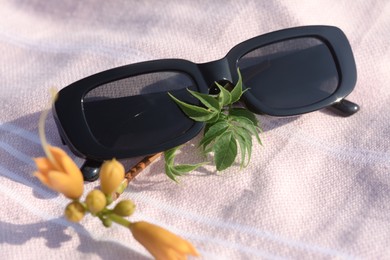 Photo of Stylish sunglasses and tropical flower on blanket, closeup