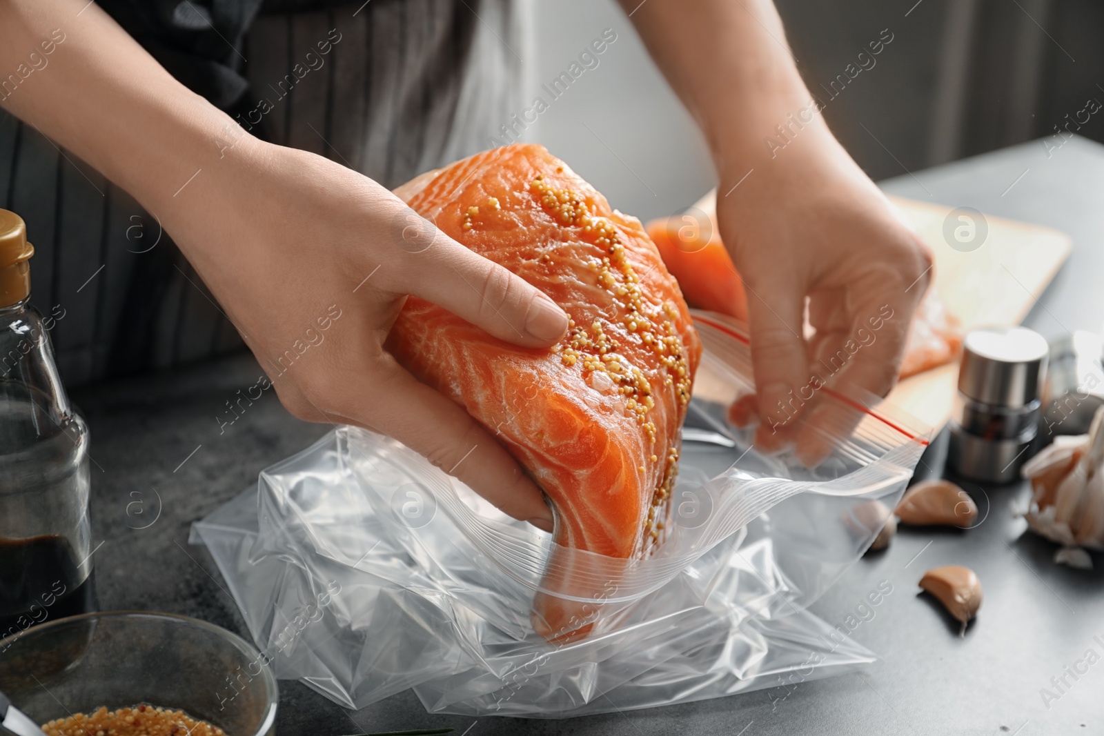 Photo of Woman putting marinated salmon fillet into plastic bag at table