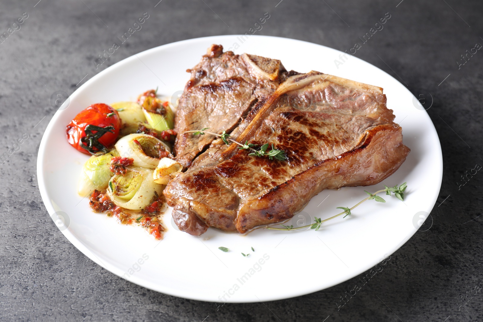 Photo of Delicious fried beef meat and vegetables on grey table