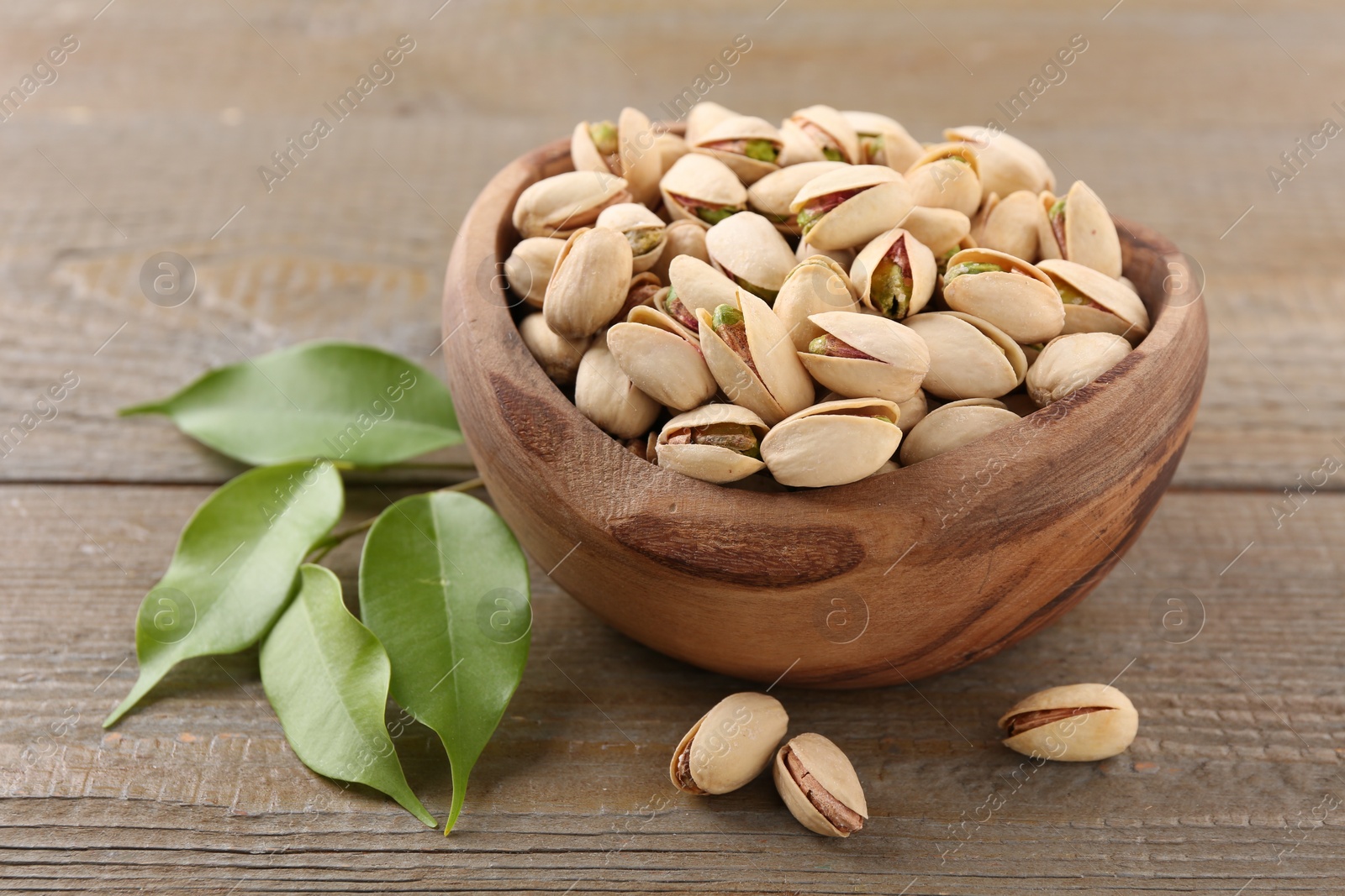 Photo of Delicious pistachios in bowl on wooden table