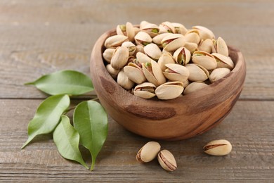 Photo of Delicious pistachios in bowl on wooden table