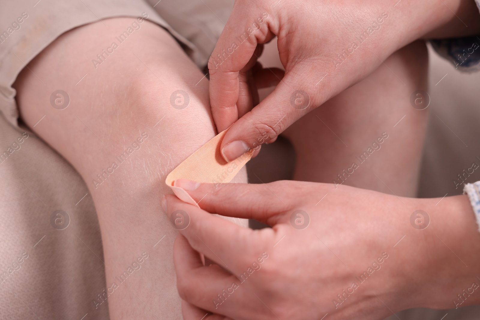 Photo of Woman putting sticking tape onto little boy`s knee on sofa, closeup