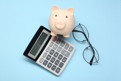 Photo of Calculator, glasses and piggy bank on light blue background, flat lay