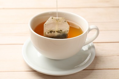 Putting tea bag in cup on light wooden table, closeup