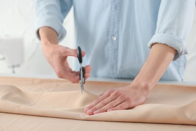 Photo of Dressmaker cutting fabric with scissors at table in atelier, closeup