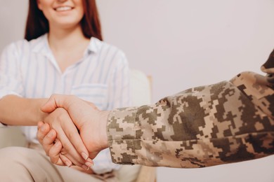 Psychologist shaking hands with military officer indoors, closeup