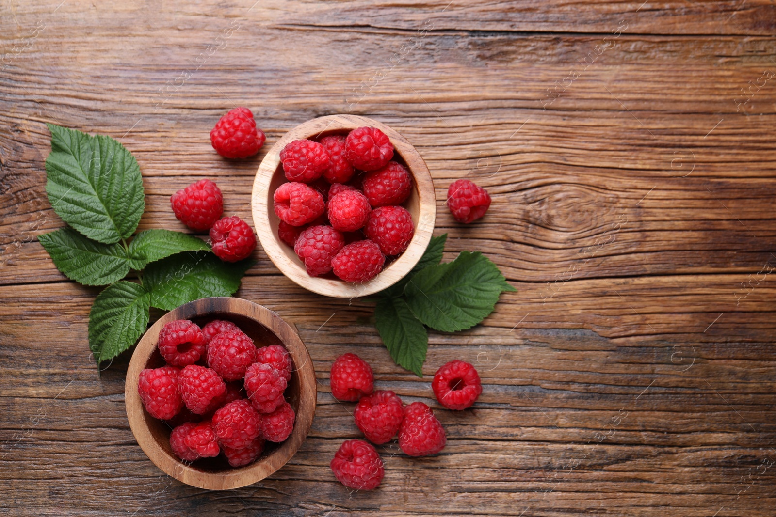 Photo of Tasty ripe raspberries and green leaves on wooden table, flat lay. Space for text