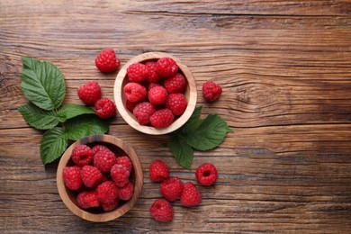 Tasty ripe raspberries and green leaves on wooden table, flat lay. Space for text