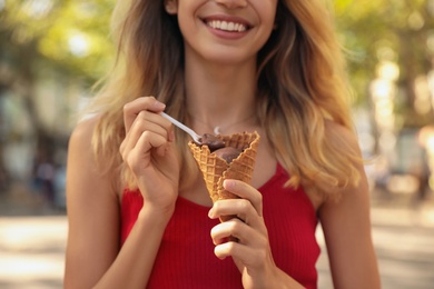 Happy young woman with delicious ice cream in waffle cone outdoors, closeup