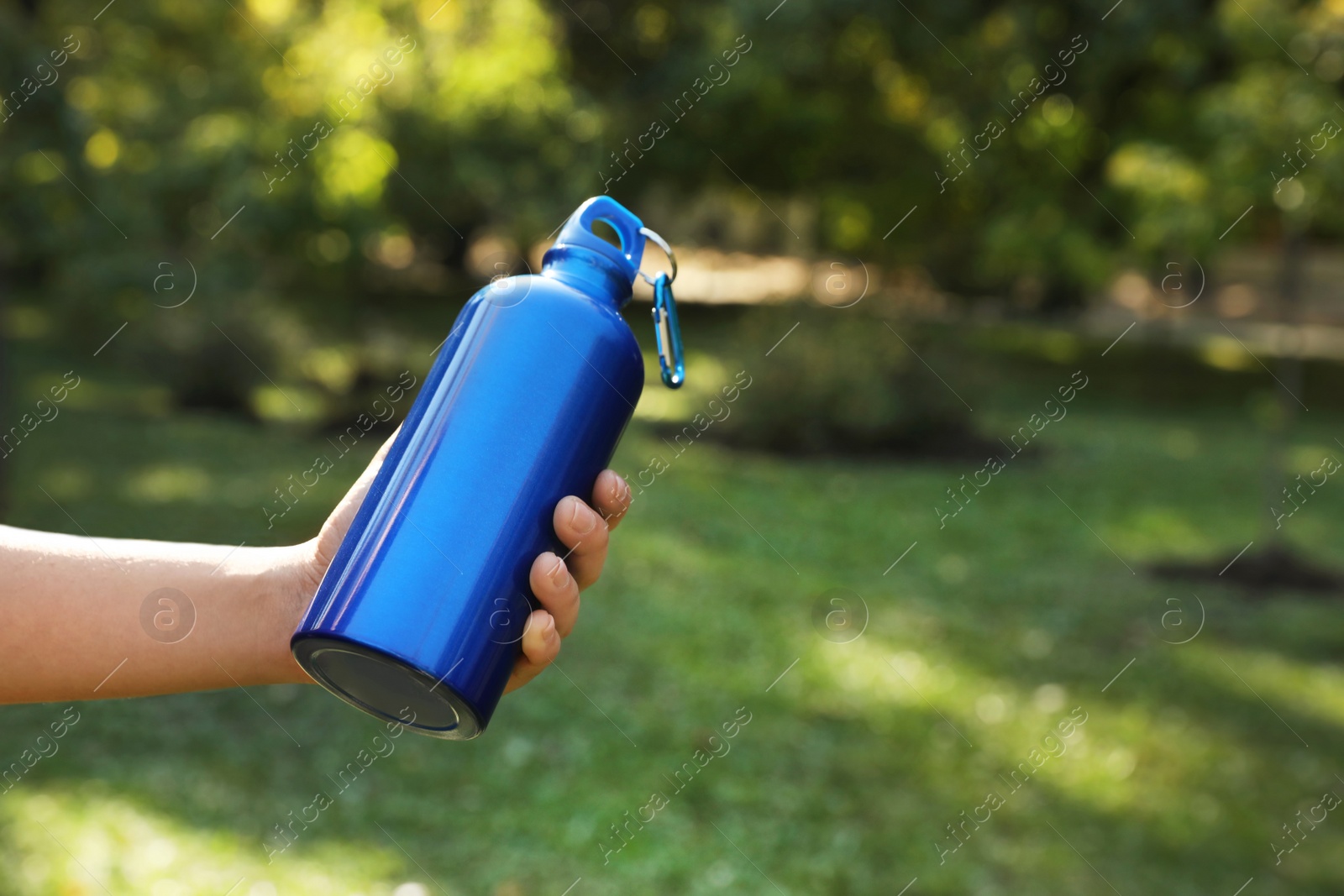 Photo of Young man holding bottle of water in park on sunny day, closeup. Space for text