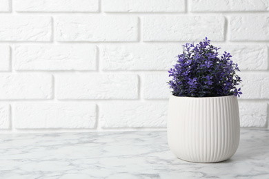 Photo of Beautiful artificial plant in flower pot on white marble table near brick wall. Space for text