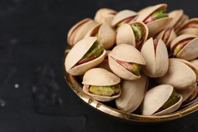 Photo of Tasty pistachios in bowl on black table, closeup. Space for text