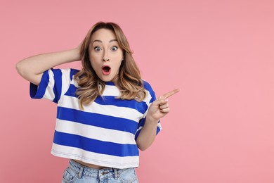 Photo of Portrait of surprised woman pointing at something on pink background. Space for text