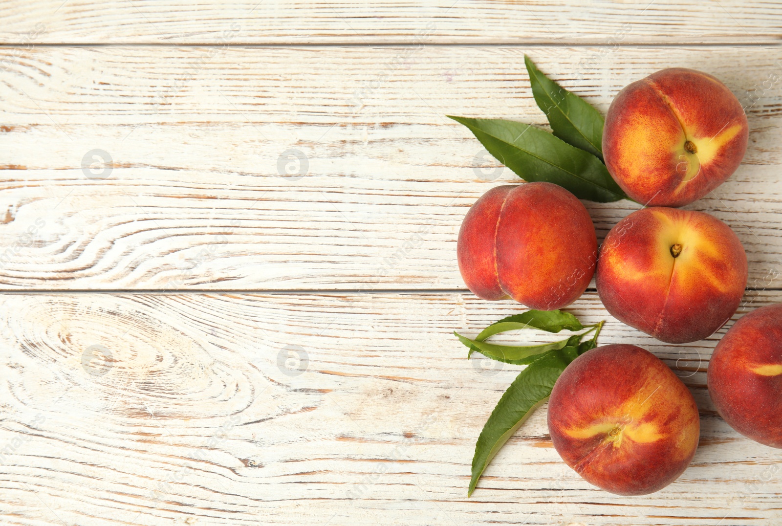 Photo of Fresh peaches and leaves on white wooden table, top view with space for text