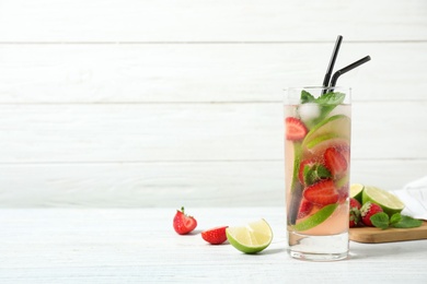 Photo of Delicious refreshing drink with strawberry and lime on white wooden table. Space for text